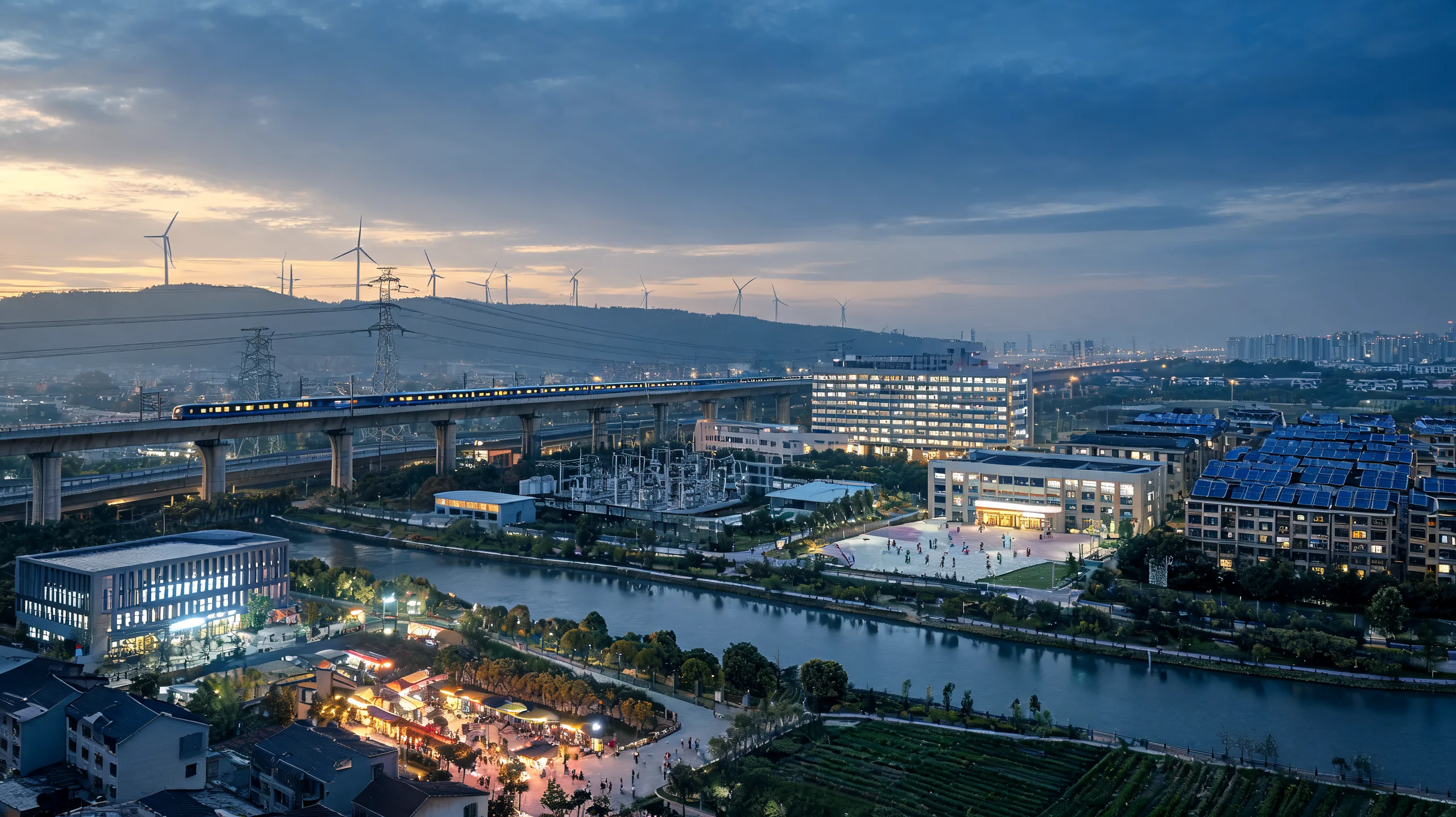One city at dusk with its systems all working at the same moment: a lit train crossing an elevated viaduct, an electrical substation, transmission lines running out to wind turbines on the ridge, a hospital block with its windows lit, a school courtyard with children still on it, solar panels across a neighbourhood of rooftops, a clean river with a planted promenade, a lit market street, and cultivated fields at the city's edge.